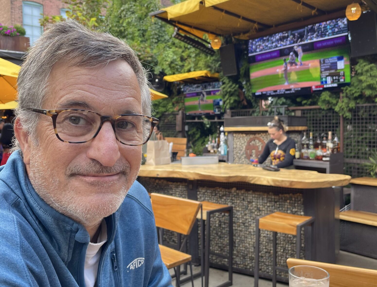 Michael Griffith, a white man with gray hair and 5-o-clock shadow, wears glasses and sits at an outdoor bar. He smiles.