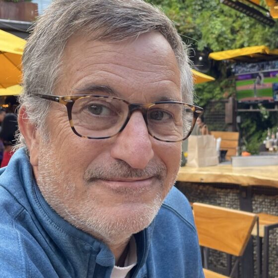 Michael Griffith, a white man with gray hair and 5-o-clock shadow, wears glasses and sits at an outdoor bar. He smiles.