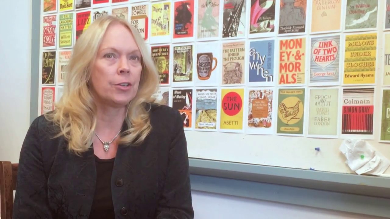Kristen Iverson, a white woman with blond hair, stands in front of a display of book covers. She appears to be speaking to someone.