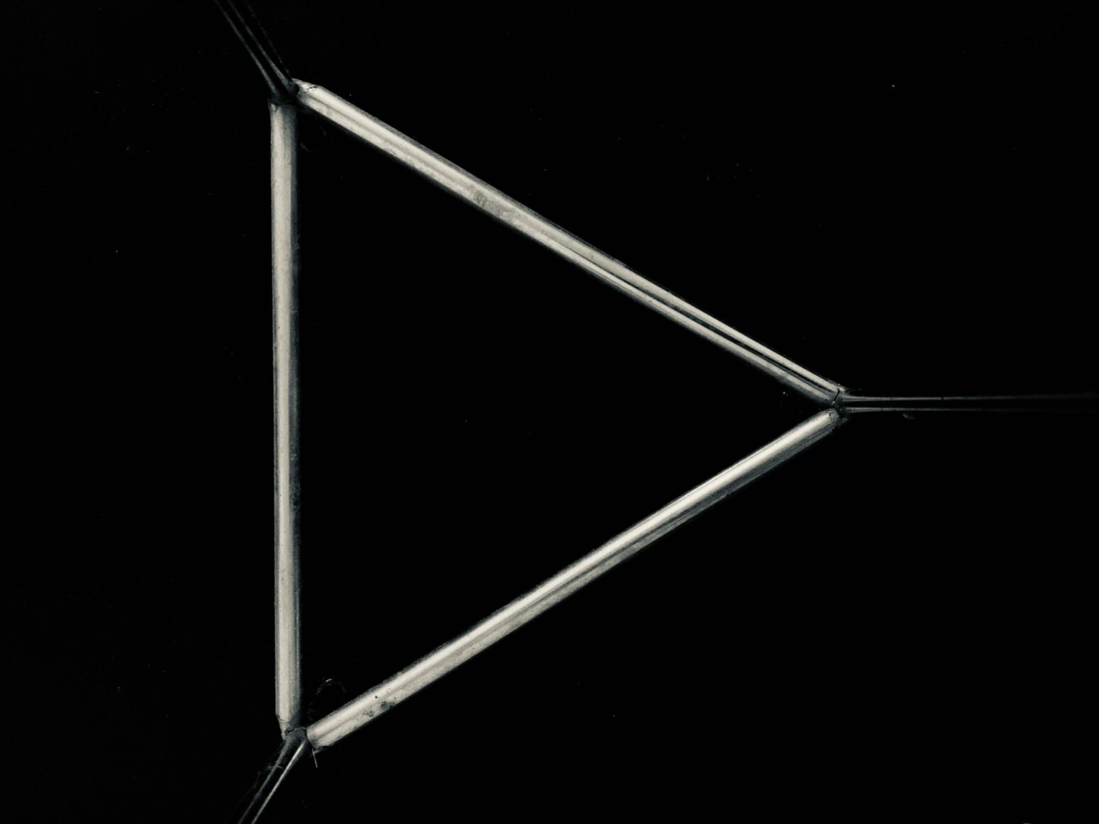 An isoceles triangle made of metal, with darkness/blackness behind it