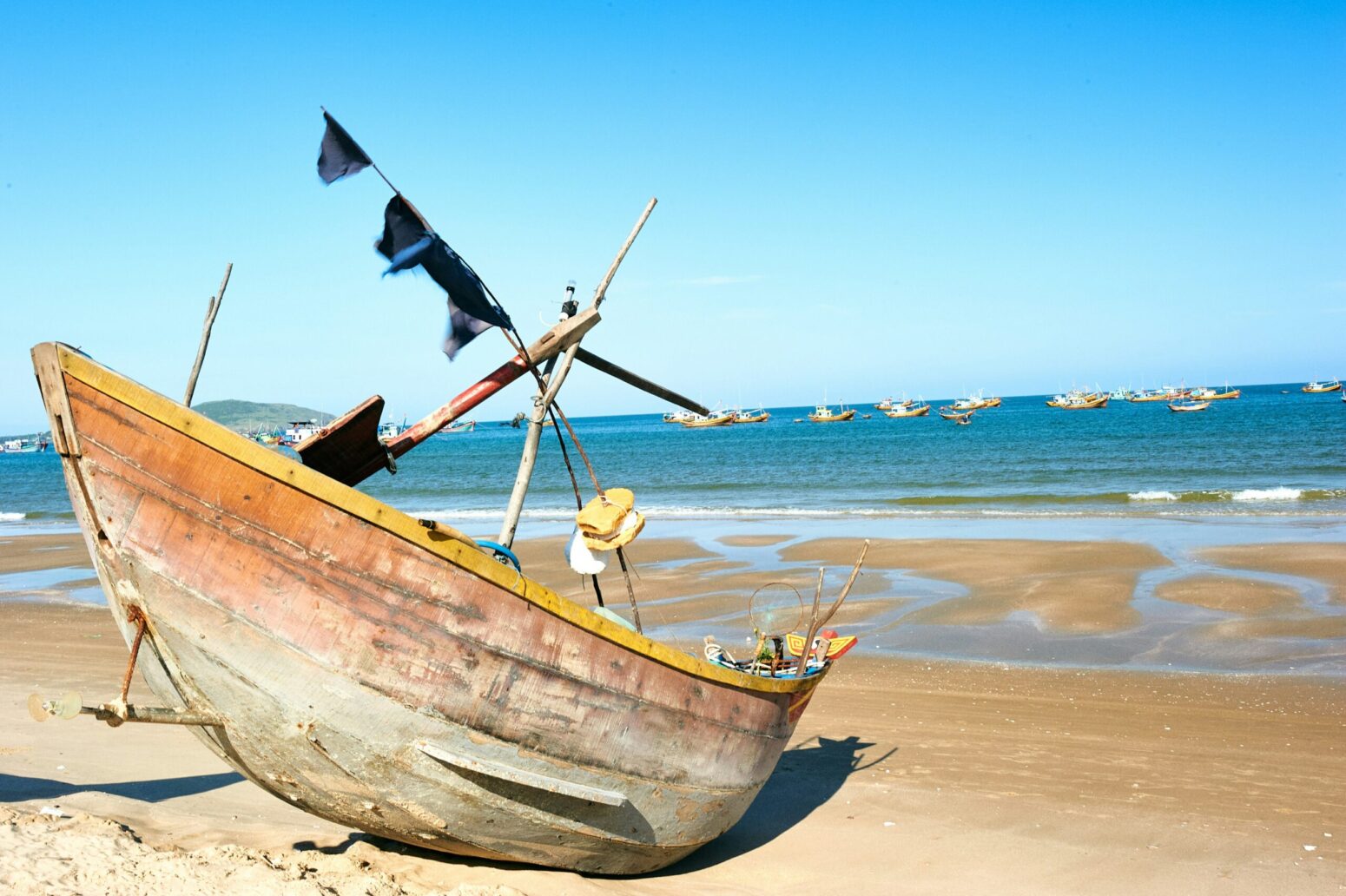 A weathered fishing boat rests on a sandy beach.