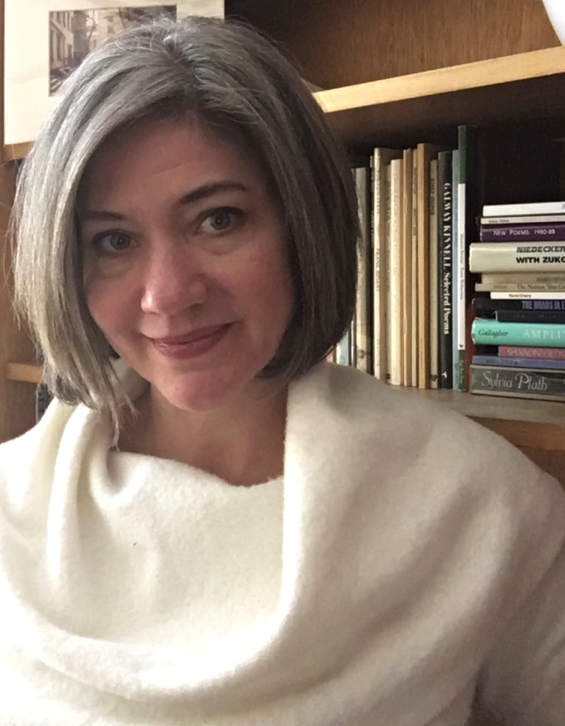 Rebecca Lindenberg, in a white cowl-neck sweater, in front of bookshelves