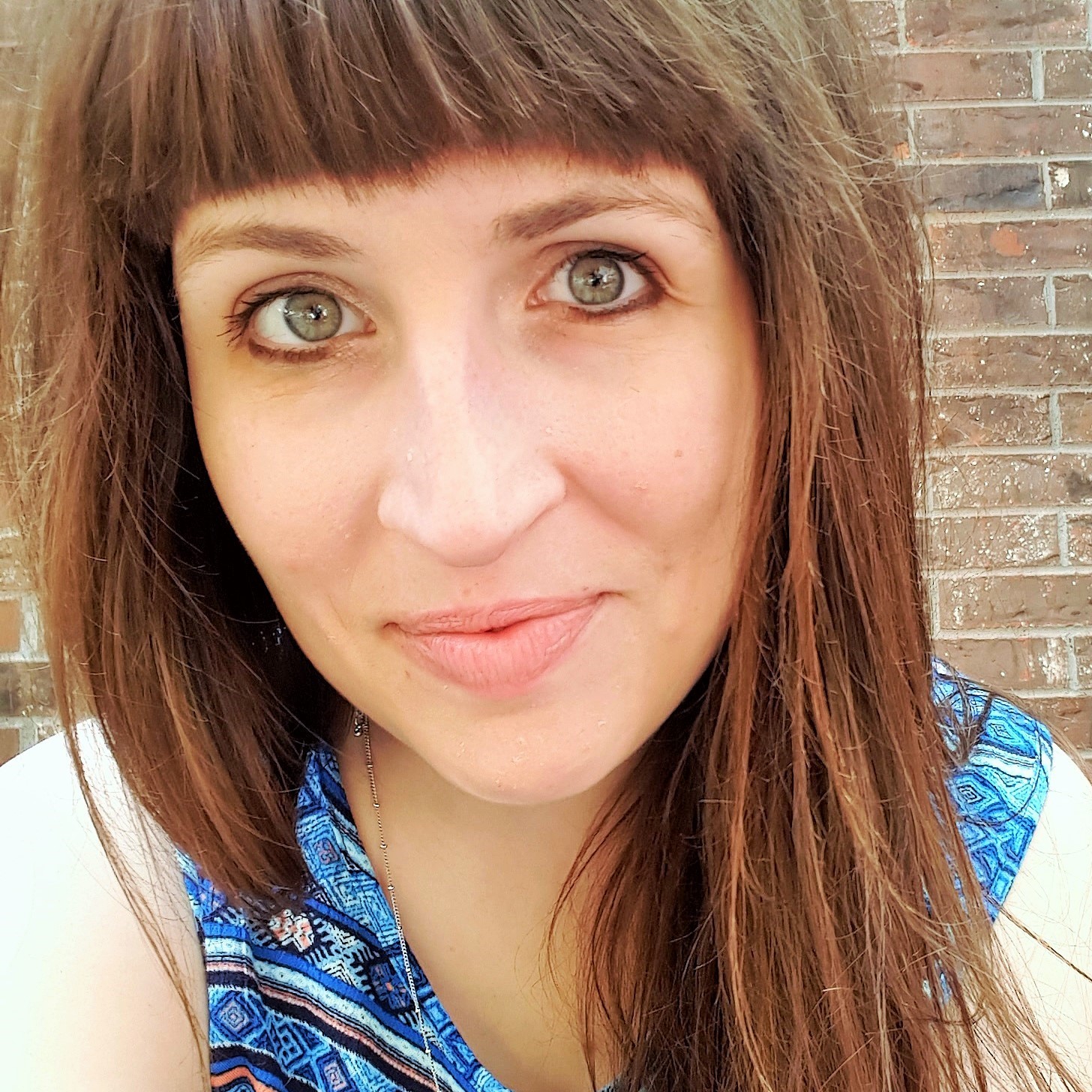Margaret Emma Brandl, a white woman with brown hair with bangs, smiles in front of a brick wall.