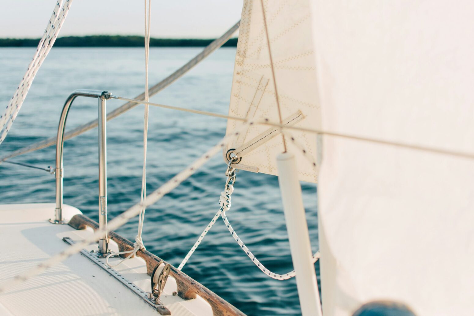 A sail and ropes on the edge of a boat, with a body of water beyond that