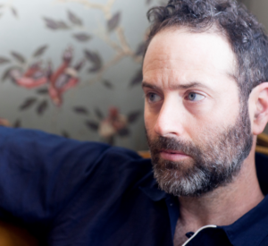 Dan O'Brien in a blue shirt, looking toward the left of the screen, with floral wallpaper