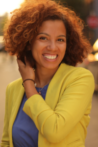 Tanya Everett in a yellow sweater and blue shirt, with her hand touching the right side of her hair