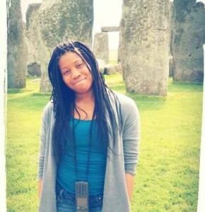 Jeneé Skinner in a gray sweater and blue T-shirt, with Stonehenge behind her