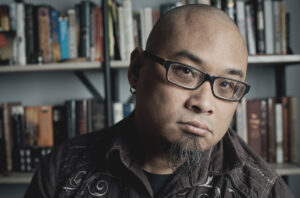 W. Todd Kaneko, with a goatee and glasses, in front of bookshelves