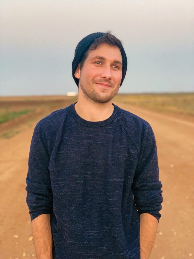 a man in a beanie on a dirt road look into the distance