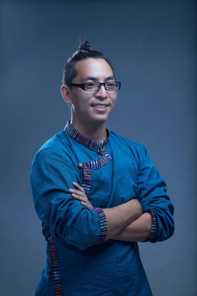 a man with his arms crossed smiles into the distance against a blue background