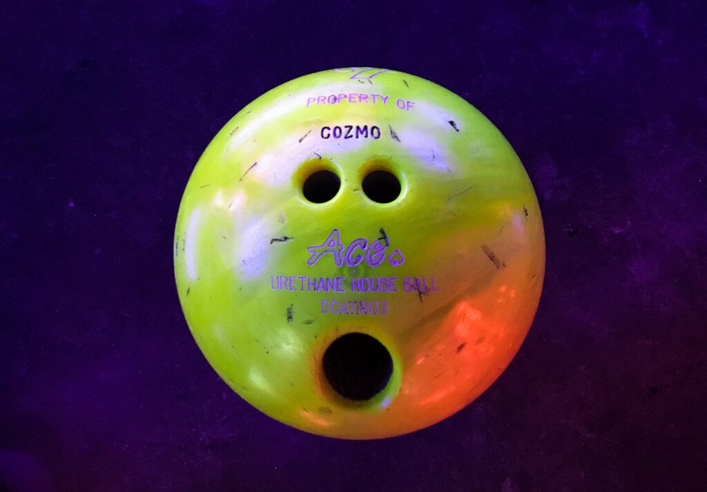 a green bowling ball positioned so that the finger holes look like a surprised face against a purple background