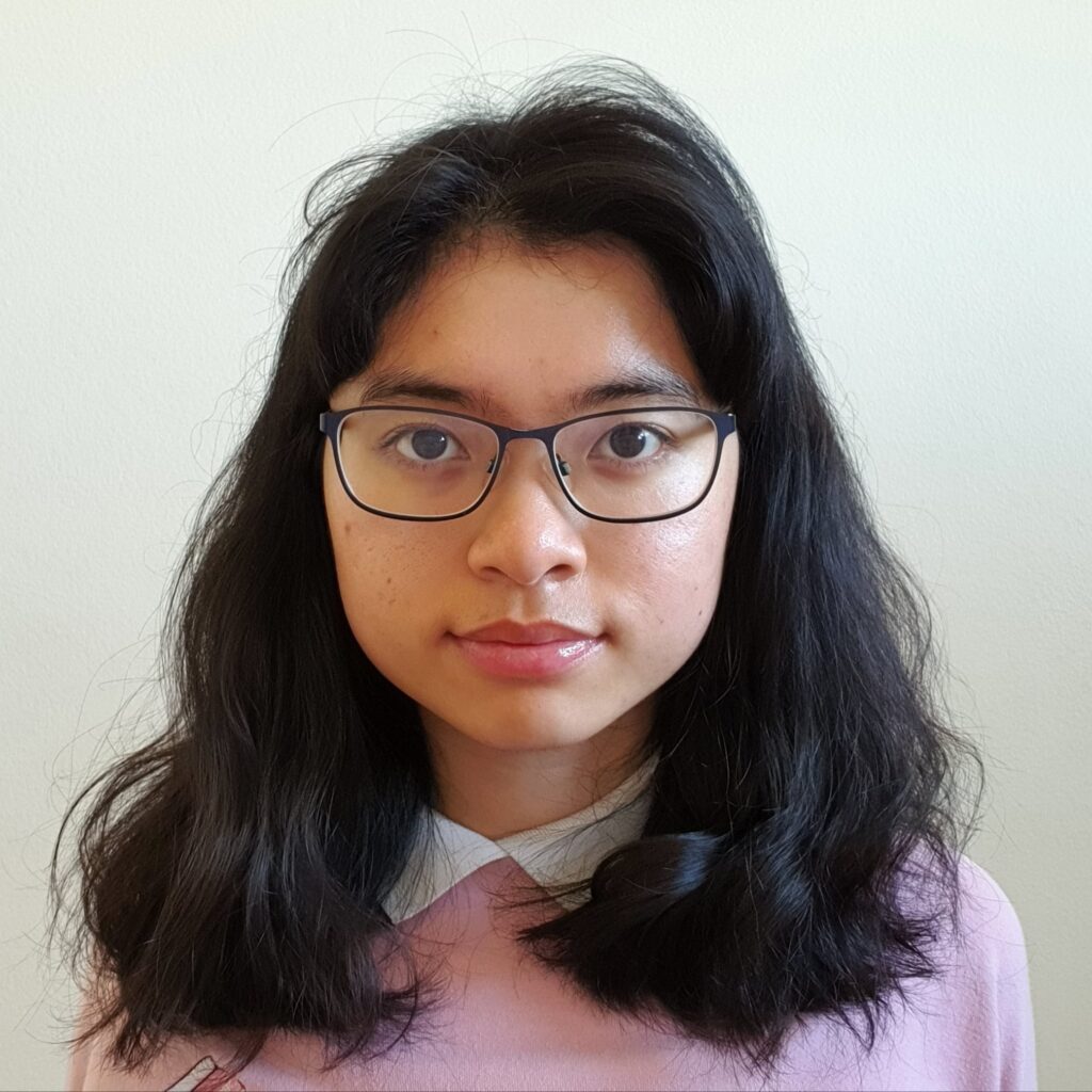 A headshot of a woman with dark hair in a pink sweater and glasses directly facing the camera