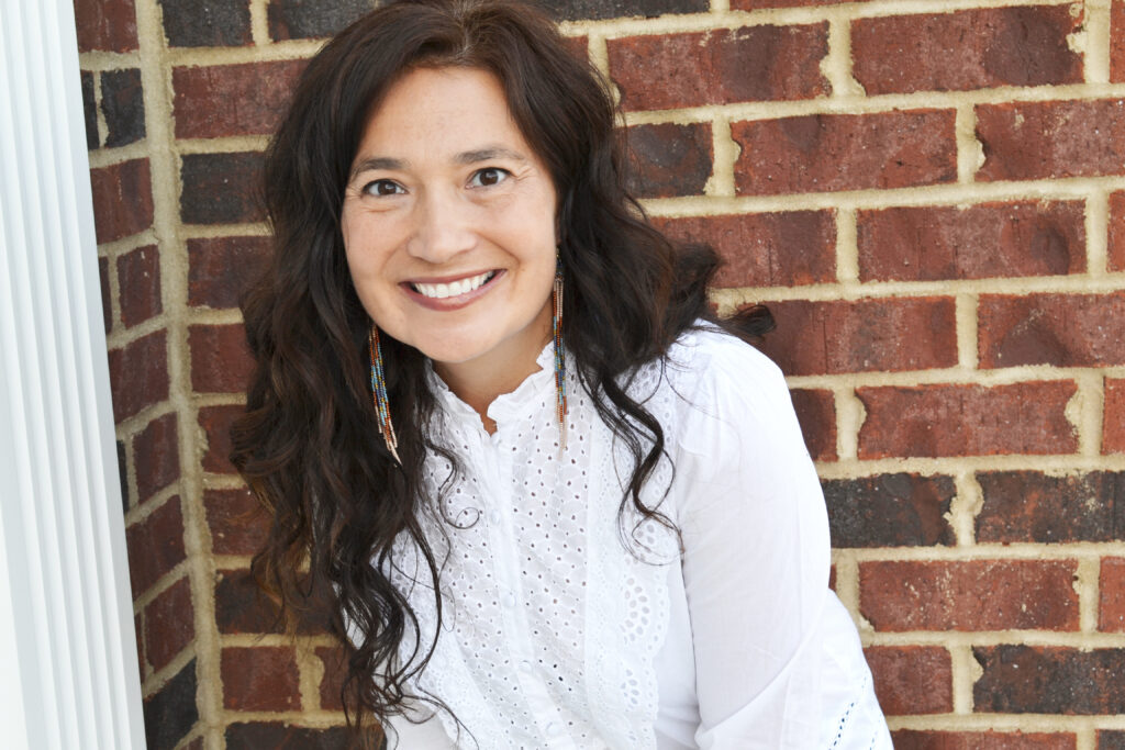 photo of author wearing a white shirt against a brick backdrop