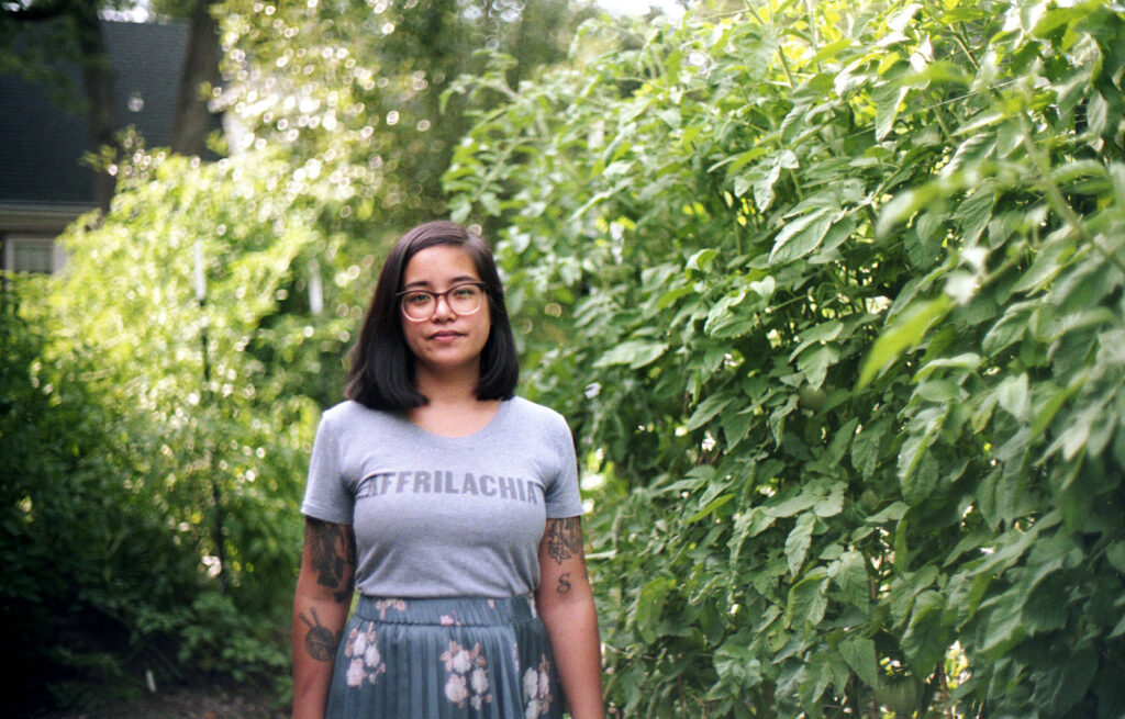 Photo of author wearing a gray t-shirt, standing in front of greenery