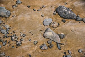 Gray stones of various sizes are pressed into brown sand. 