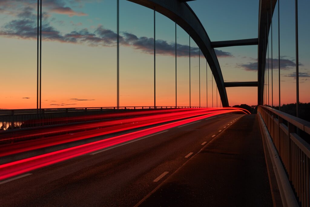 A driving bridge at sunset timelapsed so that red break lights streak across the road