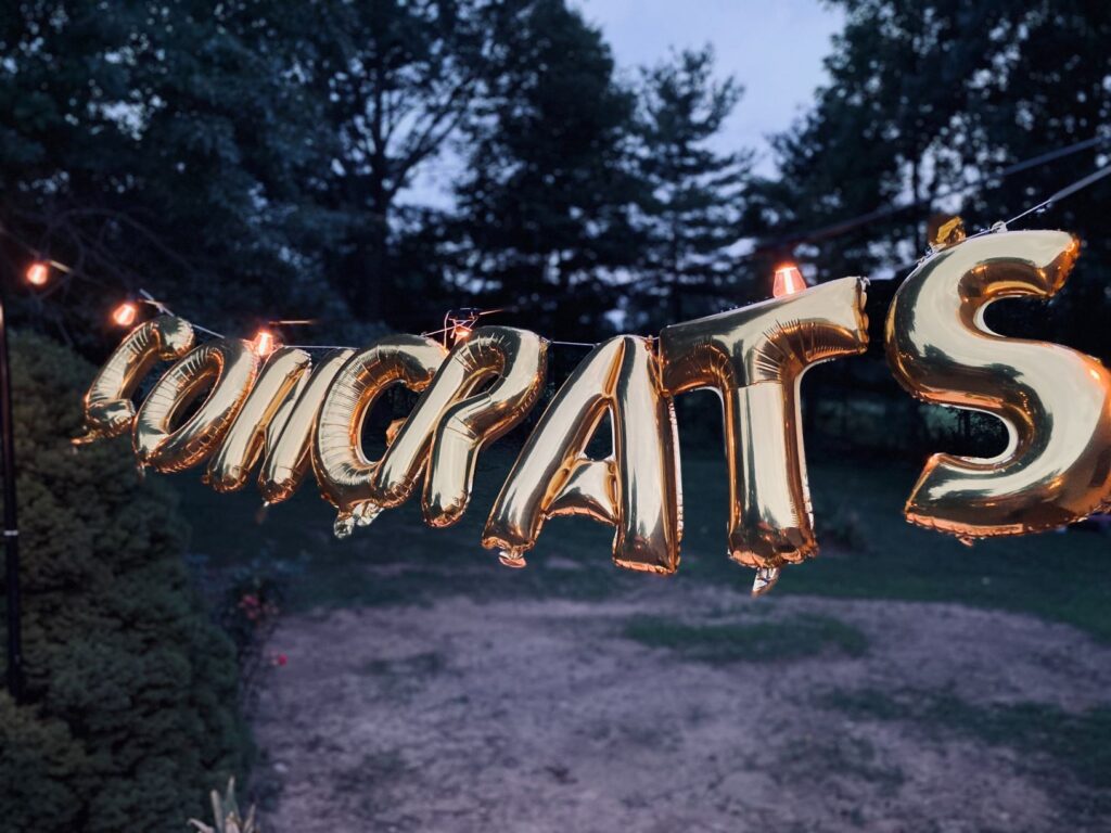 Photo of gold balloons that say "congrats" against a backdrop of trees