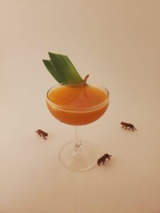 Freedom Rampage Cocktail (pre-apocalypse) sits at the center of the image with a white background. It is garnished with leaves, and three small plastic tigers circle around the stem. 