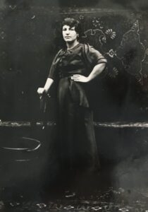 Bassiri's grandmother stands at the center of a black and white photo. One hand rests on her hip and the other rests on a chair. The photo is old and in black and white. 