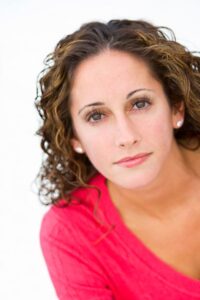 Author Melissa Bowers wears a pink shirt. Her hair is brown and curly and she looks directly into the camera. 