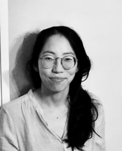 black and white headshot of a woman with black hair and glasses smiling at the camera