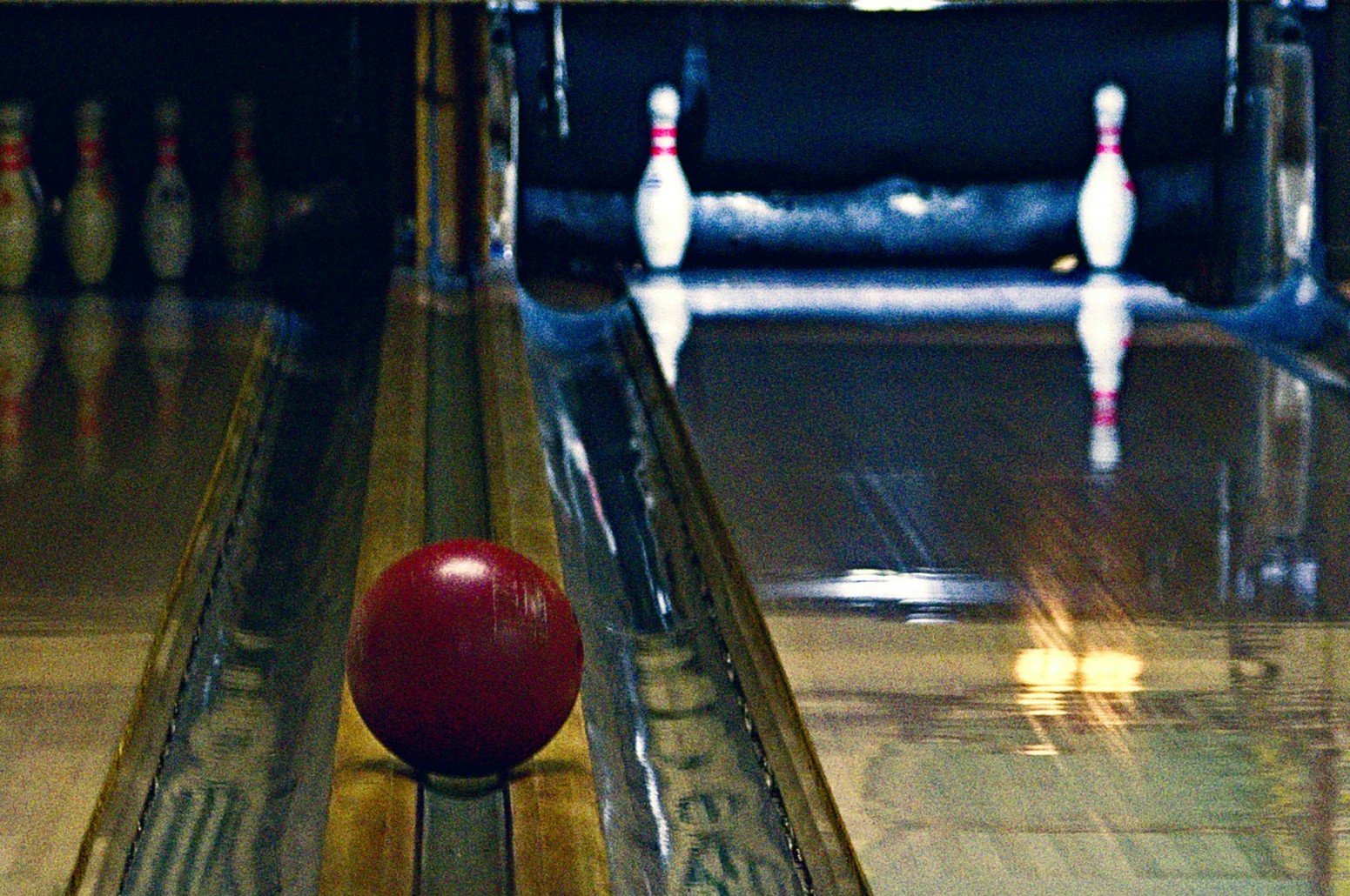 A red bowling ball rolling down the gutter at a bowling lane. The bowling pins are in a 7-10 split.