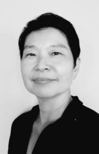 Author Amy Chen looks into the camera with a small smile. Her hair is in a pixie style and she wears a dark collared shirt. 