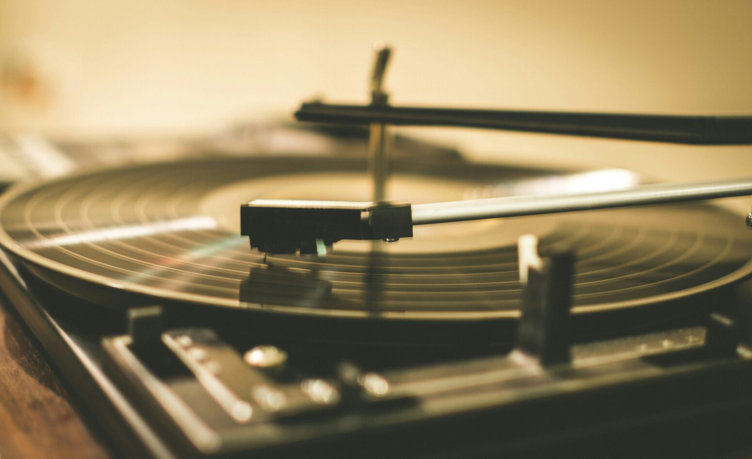 A close, slightly out of focus photo of a record player, including needle. Image has a yellow filter.