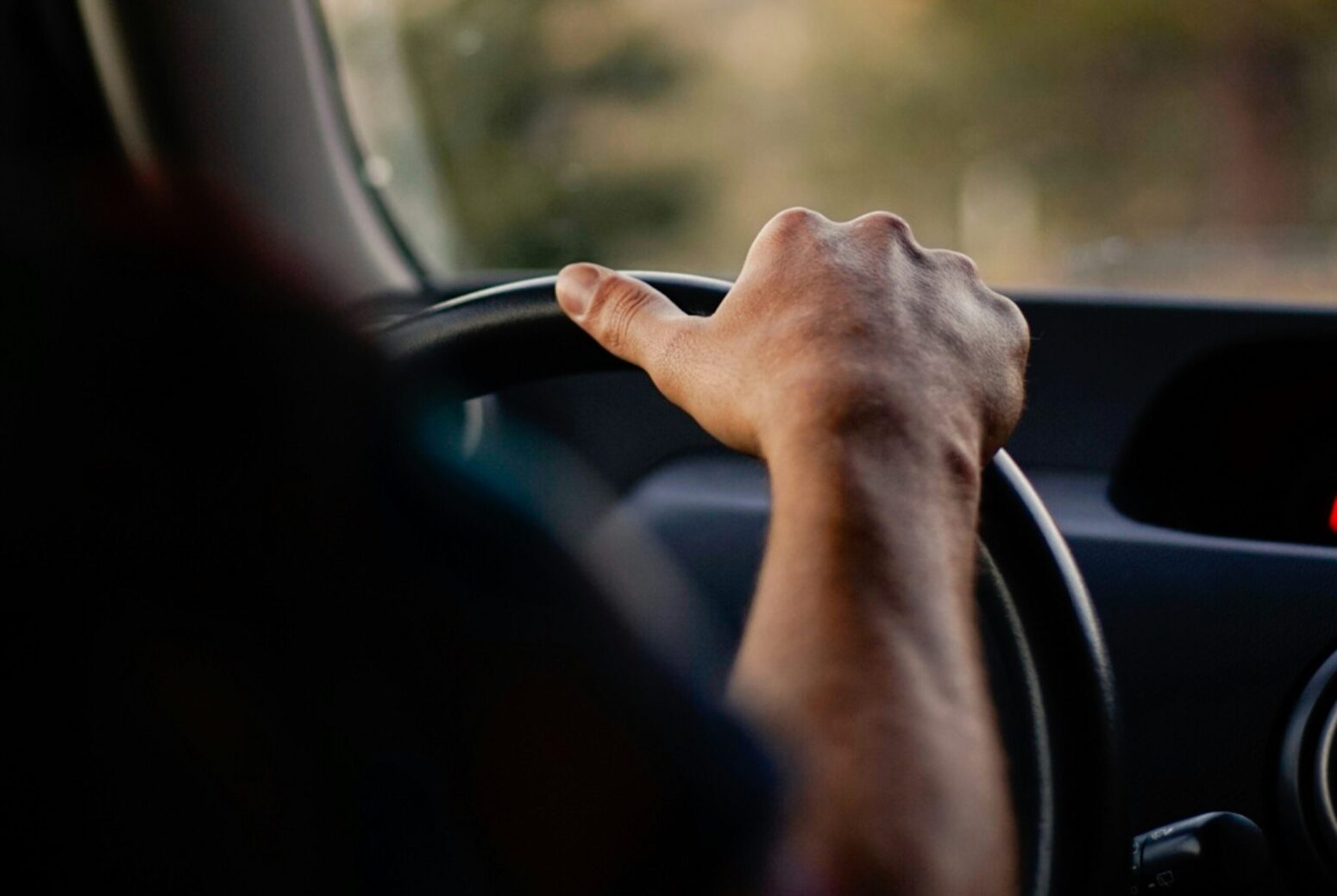 A view of a man's hand on the wheel of a car from the backseat