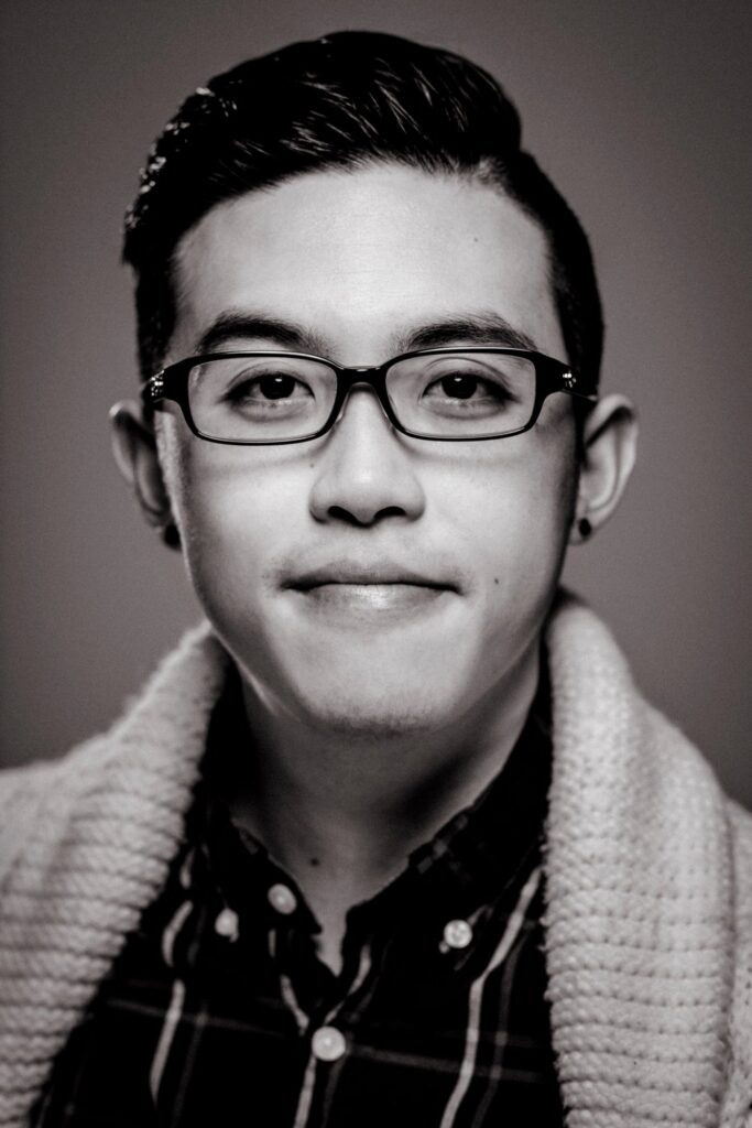 Black and white photo of author wearing glasses, a button-down, and sweater cardigan