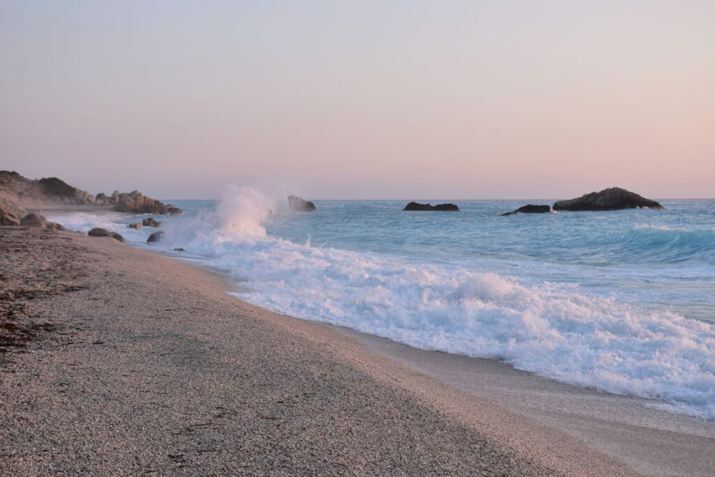 Photo of a beach with grainy sand and rocks coming out of the water in the background