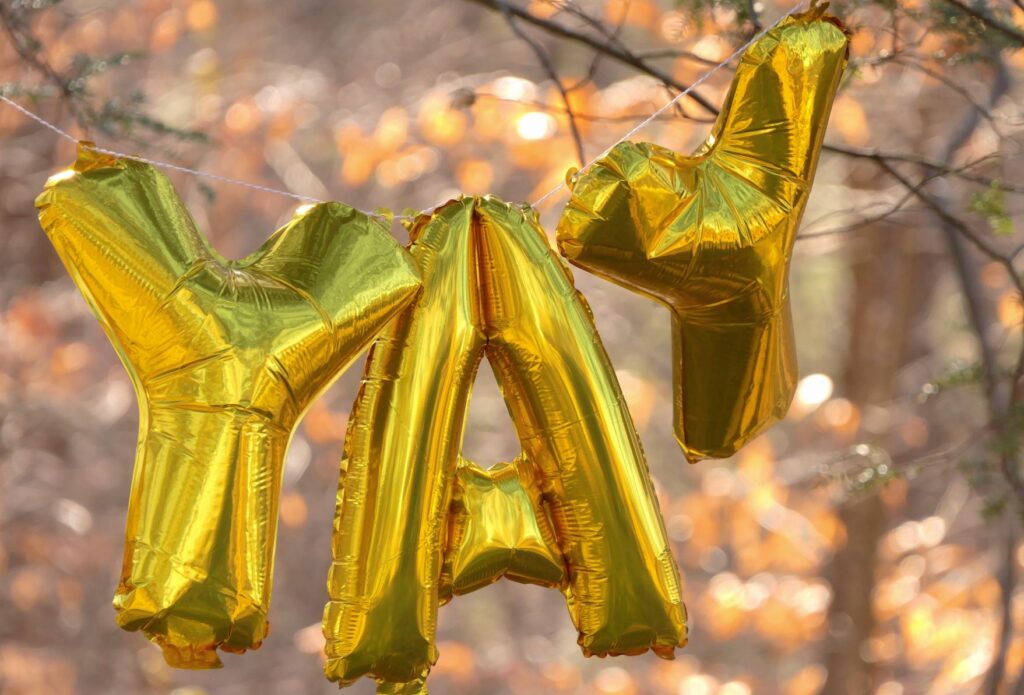 Photo of gold balloons spelling out "YAY" against a fall background of trees
