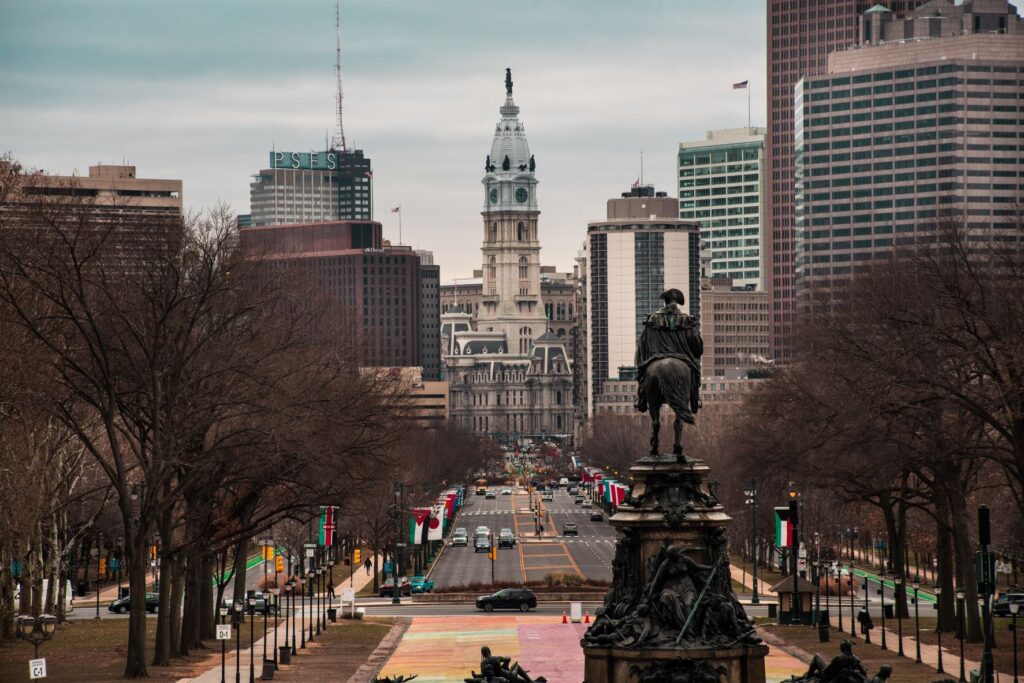 Medium-zoom photo of Philadelphia skyline, featuring the city hall, with a look down the street and trees on either side. 