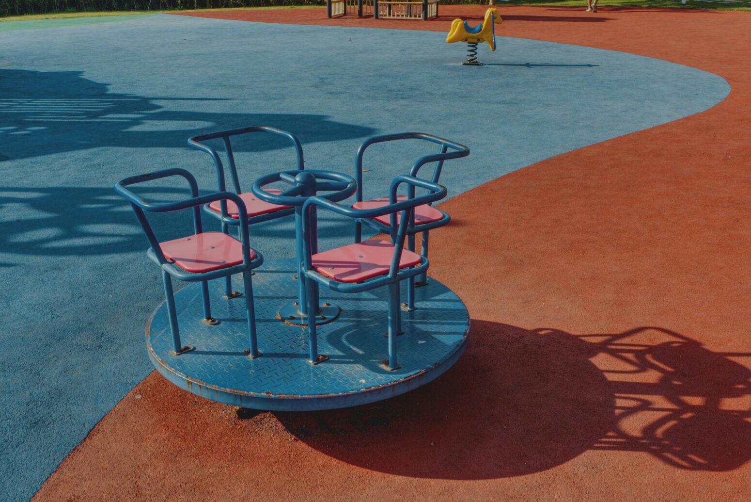 A blue and orange carpeted playground, focused on a merry go round with four blue and pink seats facing each other