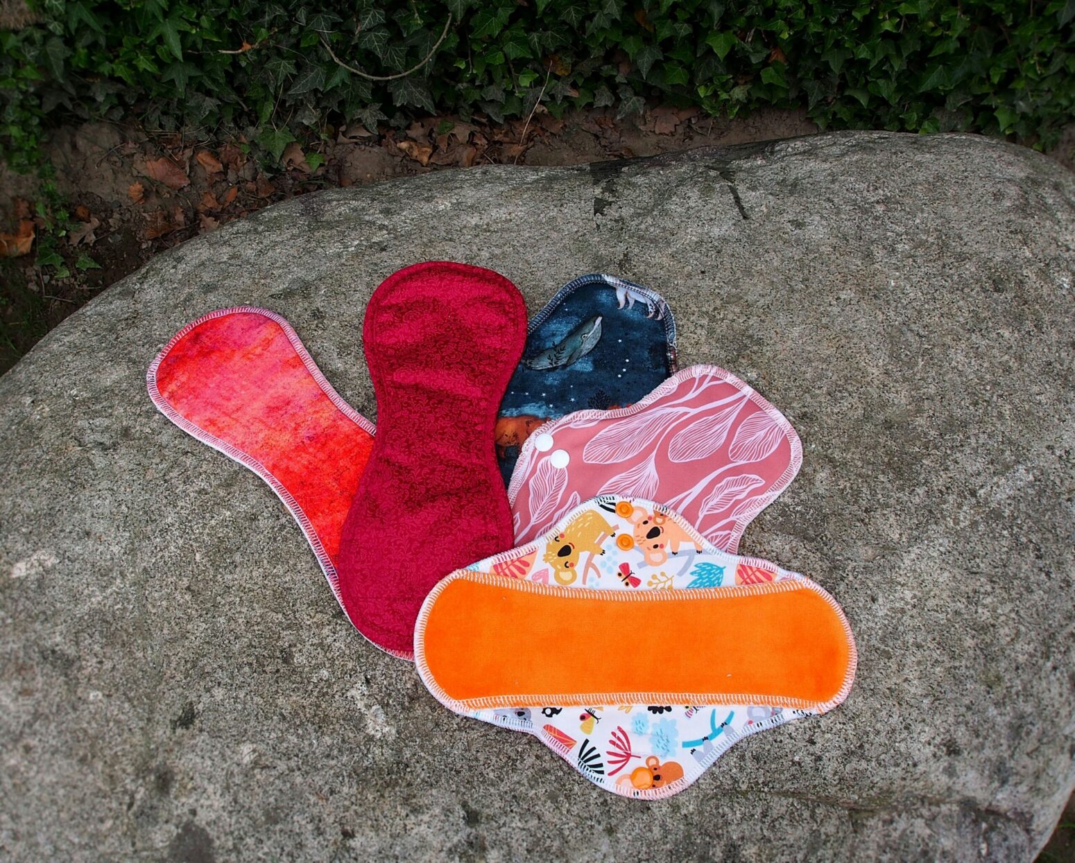 Different colors and patterns of reusable menstrual pads laying out on a rock