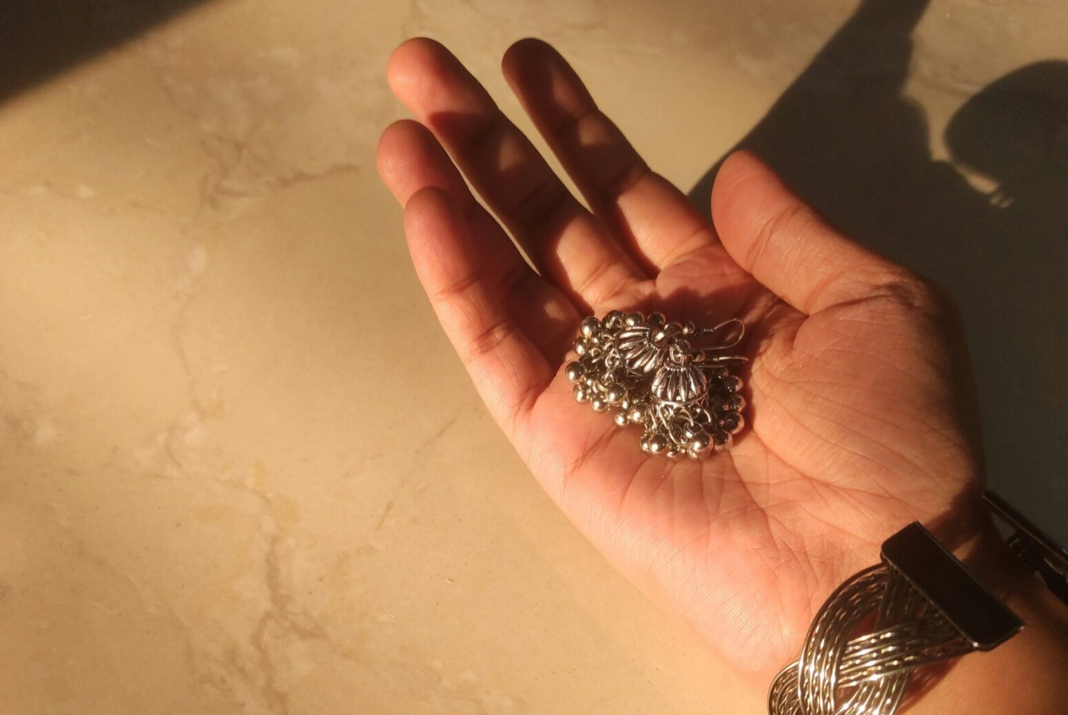 A person with a silver bracelet, holding a pair of dangly earrings in the palm of their hand.