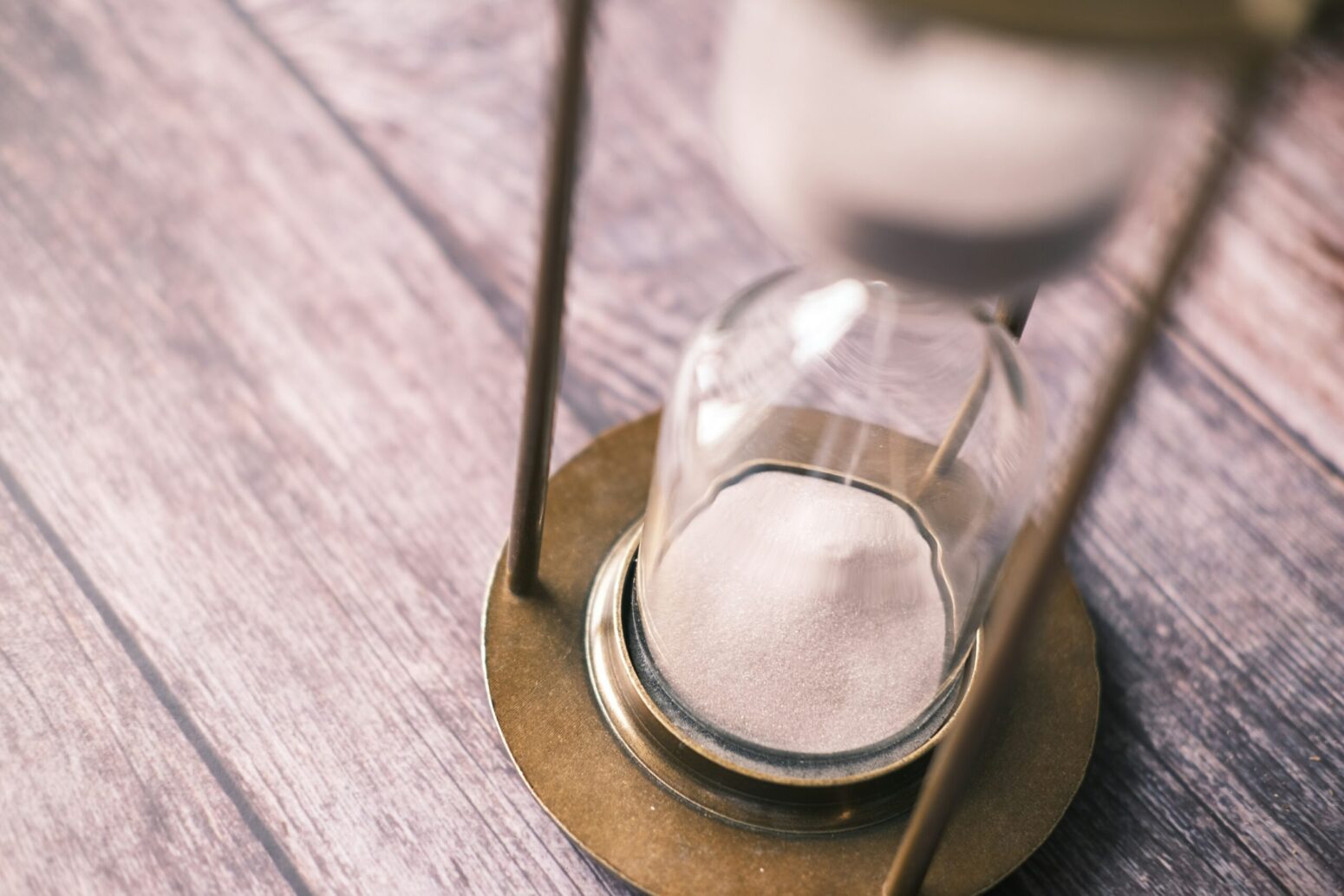 A slightly overhead view of an hourglass sitting on a wooden table