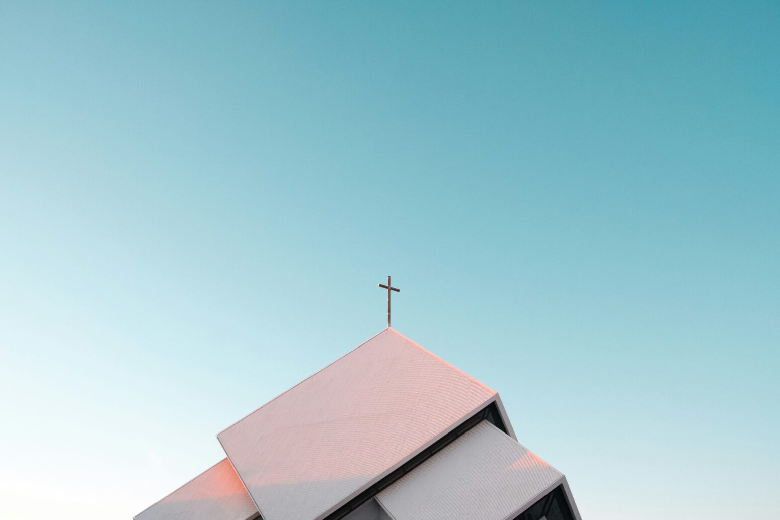 The roof of a white church against a blue sky. The church has a metal cross on the top of it.