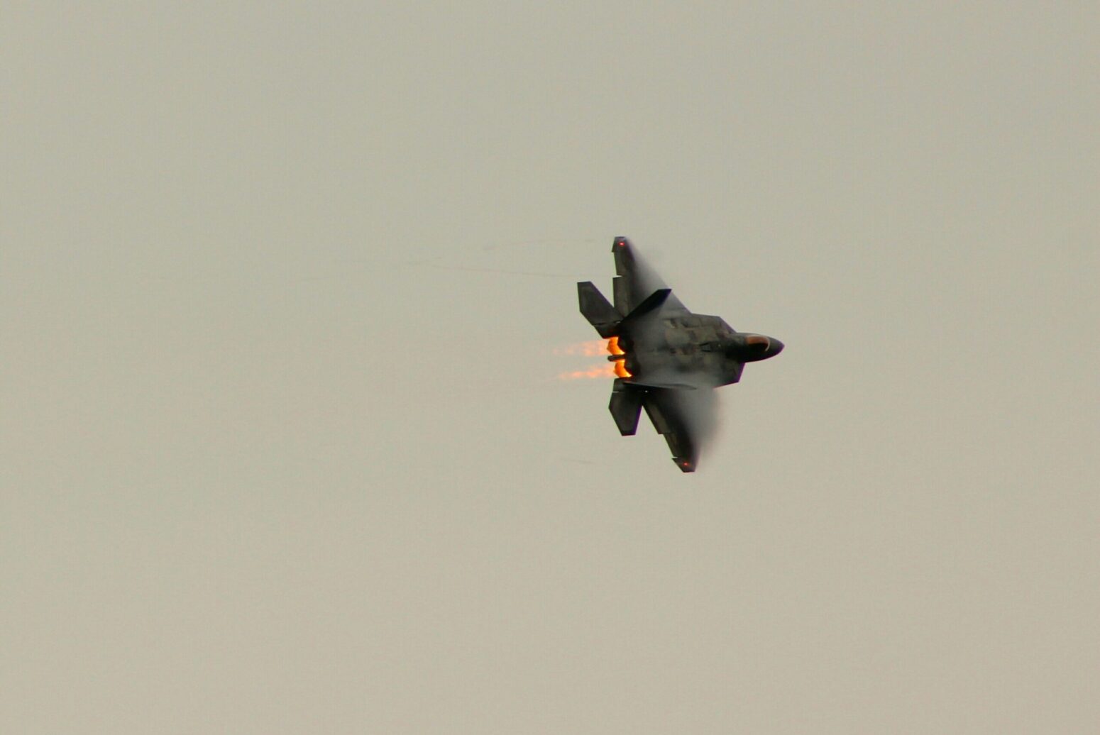 A fighter jet, turning right in a gray sky.