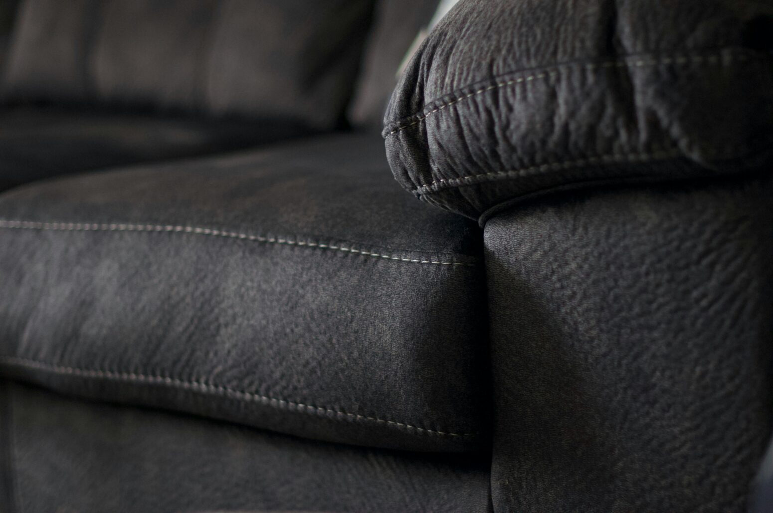 Black and white photo of the edge of a couch cushion and couch arm, slightly wrinkled leather
