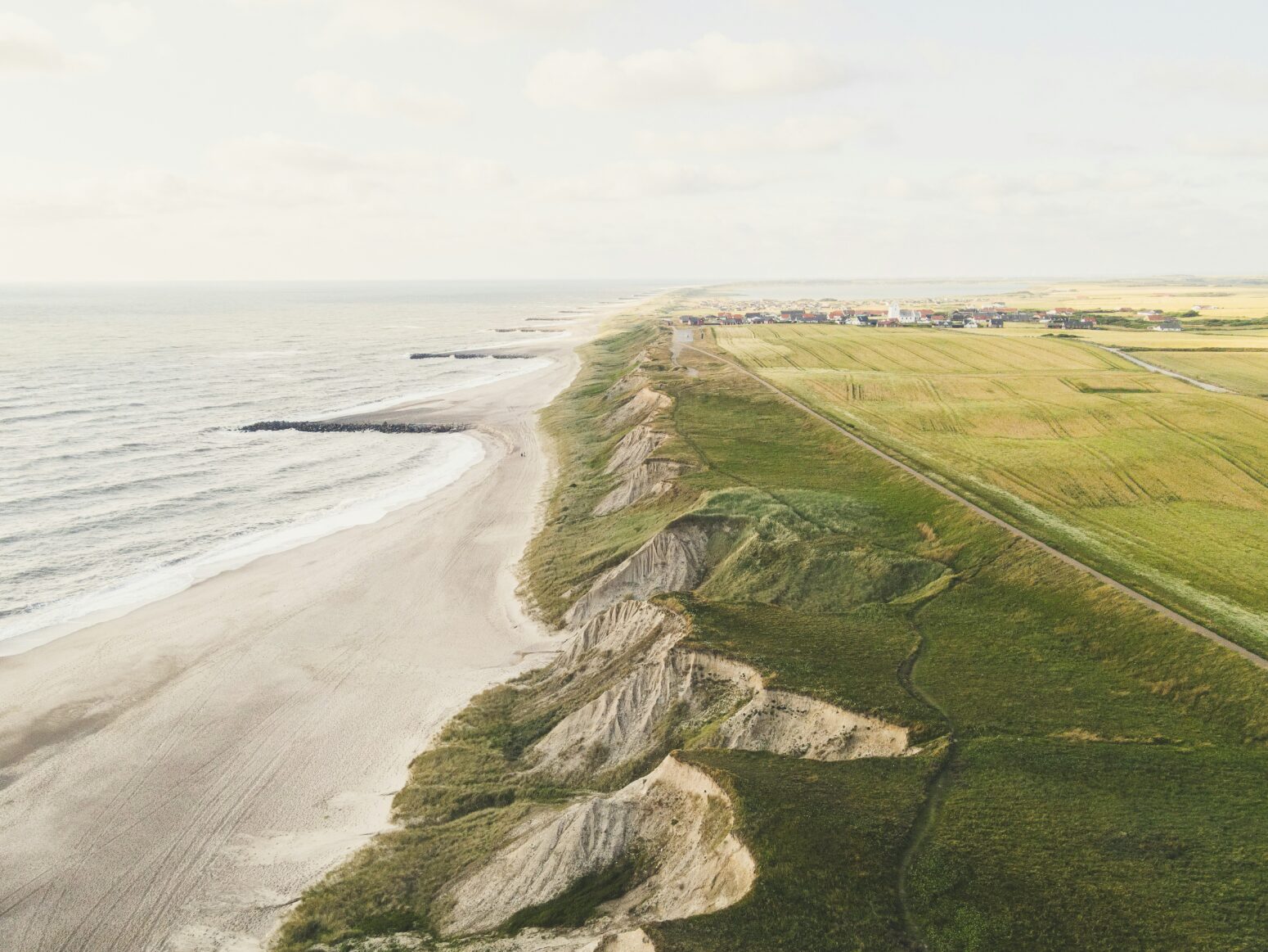 A Danish coastline, with the sea on the right, then a few sand dunes, then a small cliff with green grass on the top