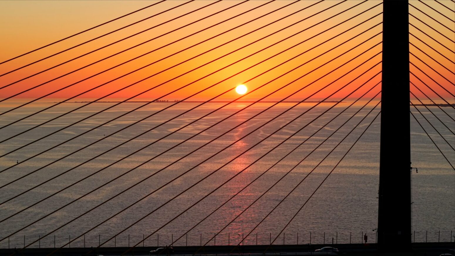 A sunset over water, seen between the suspension cords of the Sunshine Skyway bridge.