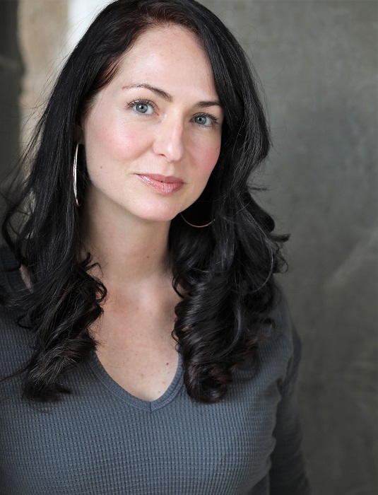 Danielle Deulen, a woman with black hair and blue eyes, is weraing a gray shirt and hoop earrings. 