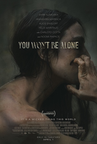 An image of a movie poster: we see a woman mostly in shadow with long dark hair from the shoulders up. She wears no clothes and has mud on her skin. Her fingernails scrape her face and are long and witchy.  
