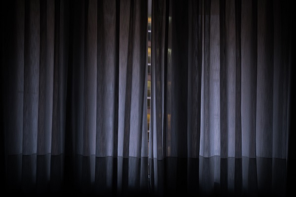A dark gray curtain with a slight opening that shows a thin slice of tiers of a theater