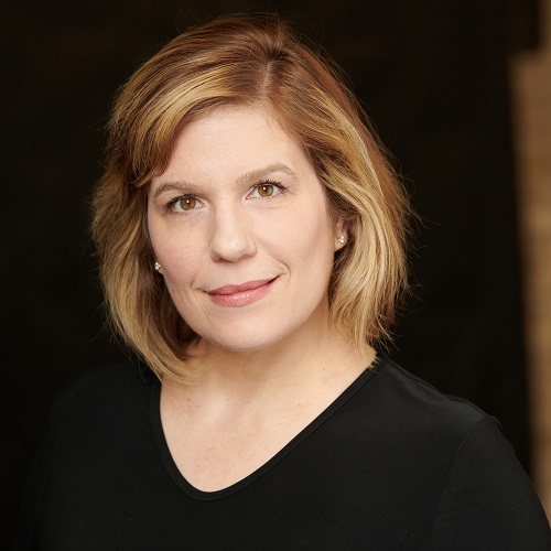 Therese Gleason, a middle-aged white woman, smiles and looks directly into the camera. She has chin length blonde hair and wears a black V-neck blouse.