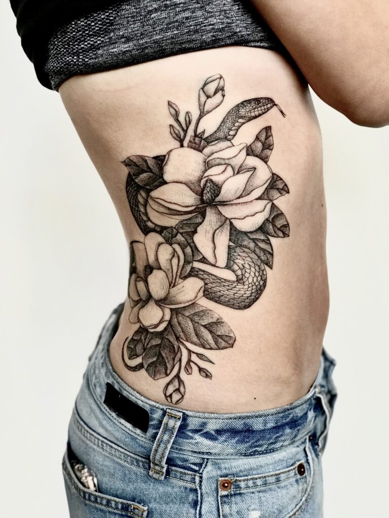 An image of a tattoo on a torso: a snake centered between flower blossoms.