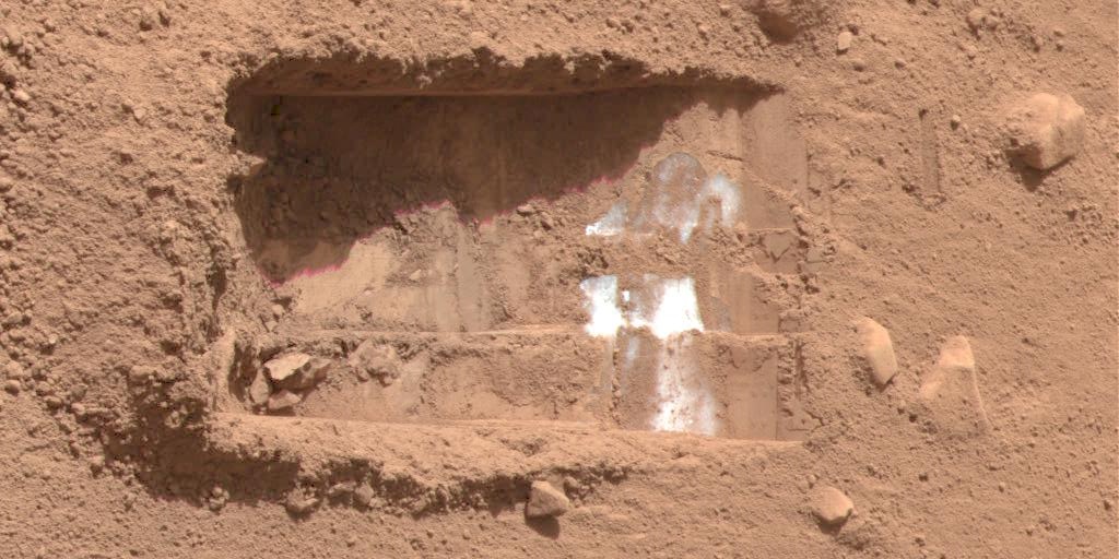 Orange-reddish sand and rocks, with a rectangular trench dug into it.