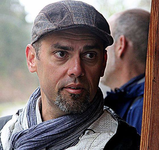 Jeremy Paden, a bearded white man wearing a striped cap and knotted scarf, looks just to the side of the camera. A wooden post appears in the edge of the frame.