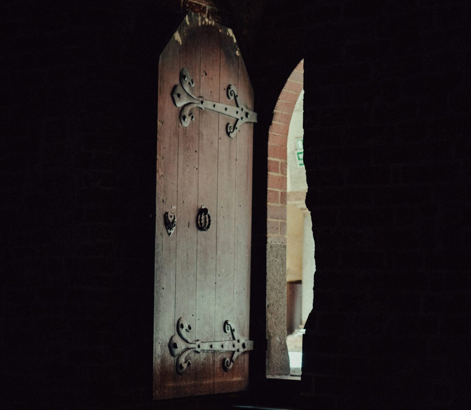 A dark entryway with a very large wooden artched door open to a sunnier place.